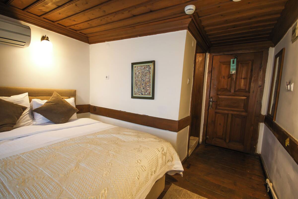 Une chambre d’hôtel avec un lit, une œuvre d’art encadrée au mur, une porte en bois et un plafond avec des poutres apparentes.