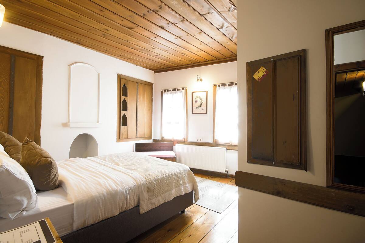 Une chambre à coucher avec un lit, un plafond en bois, des murs blancs et une fenêtre avec des rideaux.