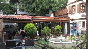 An outdoor patio area with round tables and chairs, a fountain, and a wooden fence.