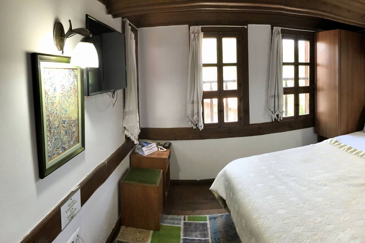 Une chambre à coucher comprenant un lit, un bureau, une chaise, une fenêtre avec des rideaux et un appareil de climatisation.