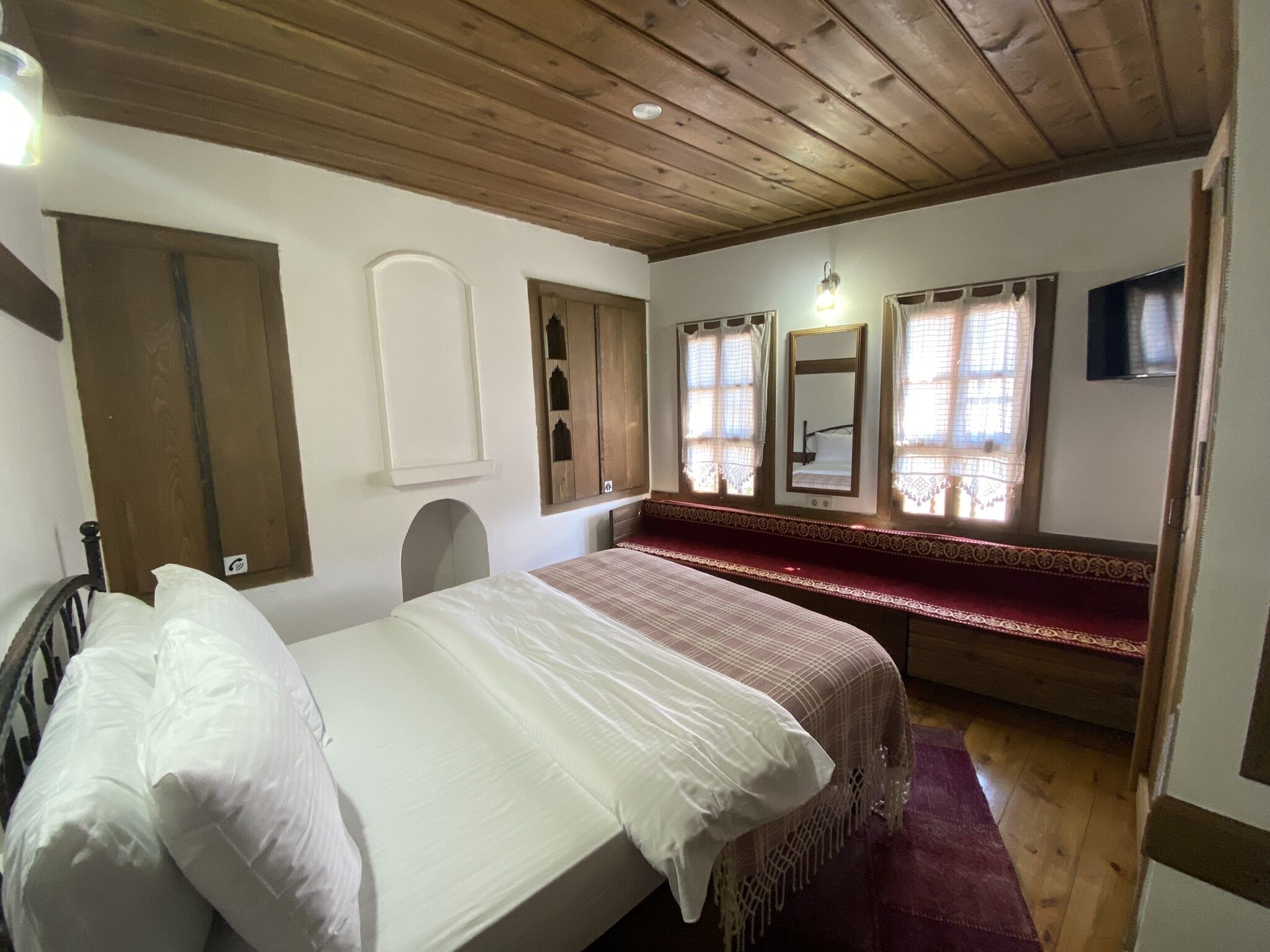 A bedroom with a wooden ceiling, a bed with white bedding, a bench, and a television.