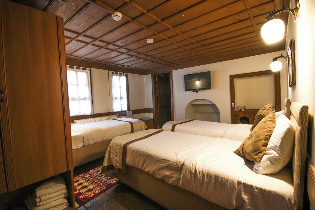 Une chambre avec deux lits, des poutres apparentes en bois au plafond, une télévision et une fenêtre avec des rideaux.