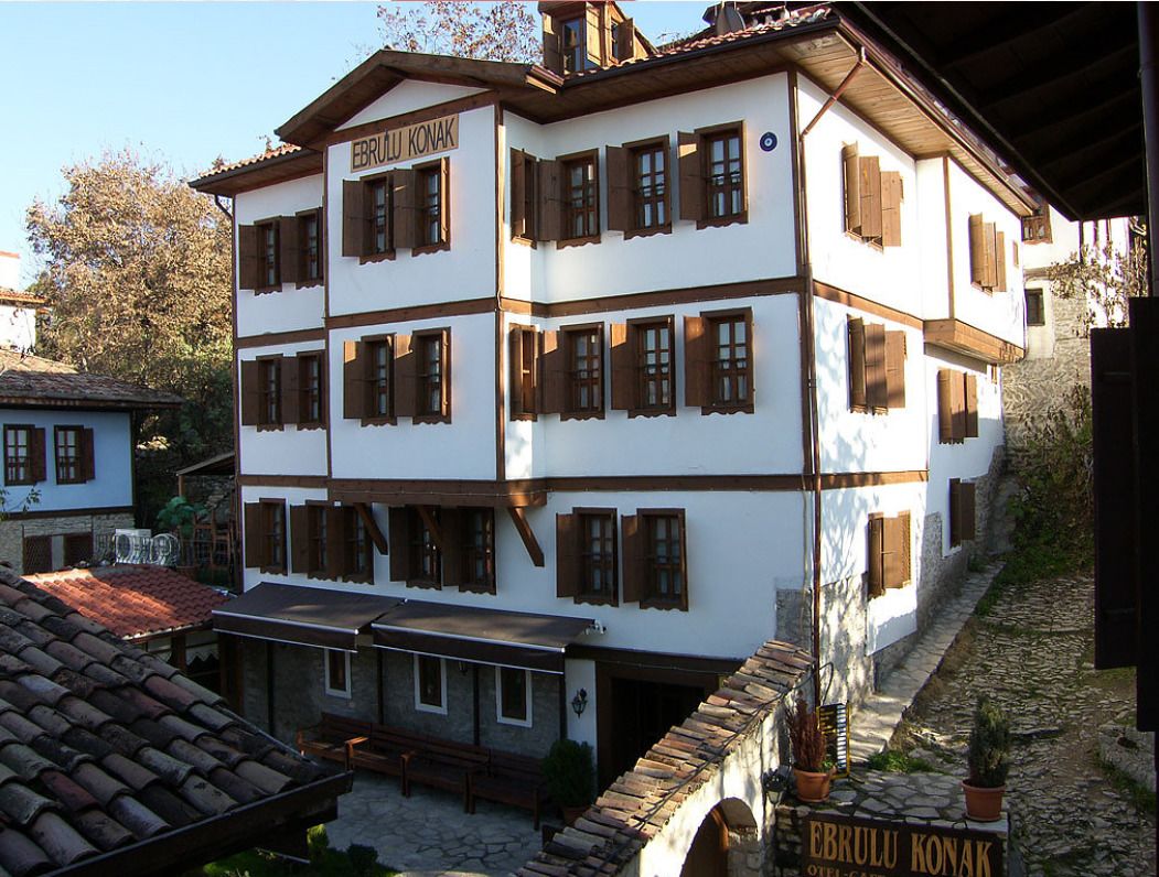Un edificio tradicional de varios pisos con un letrero que dice “EBRULU KONAK” y un arco de piedra que da a un patio.