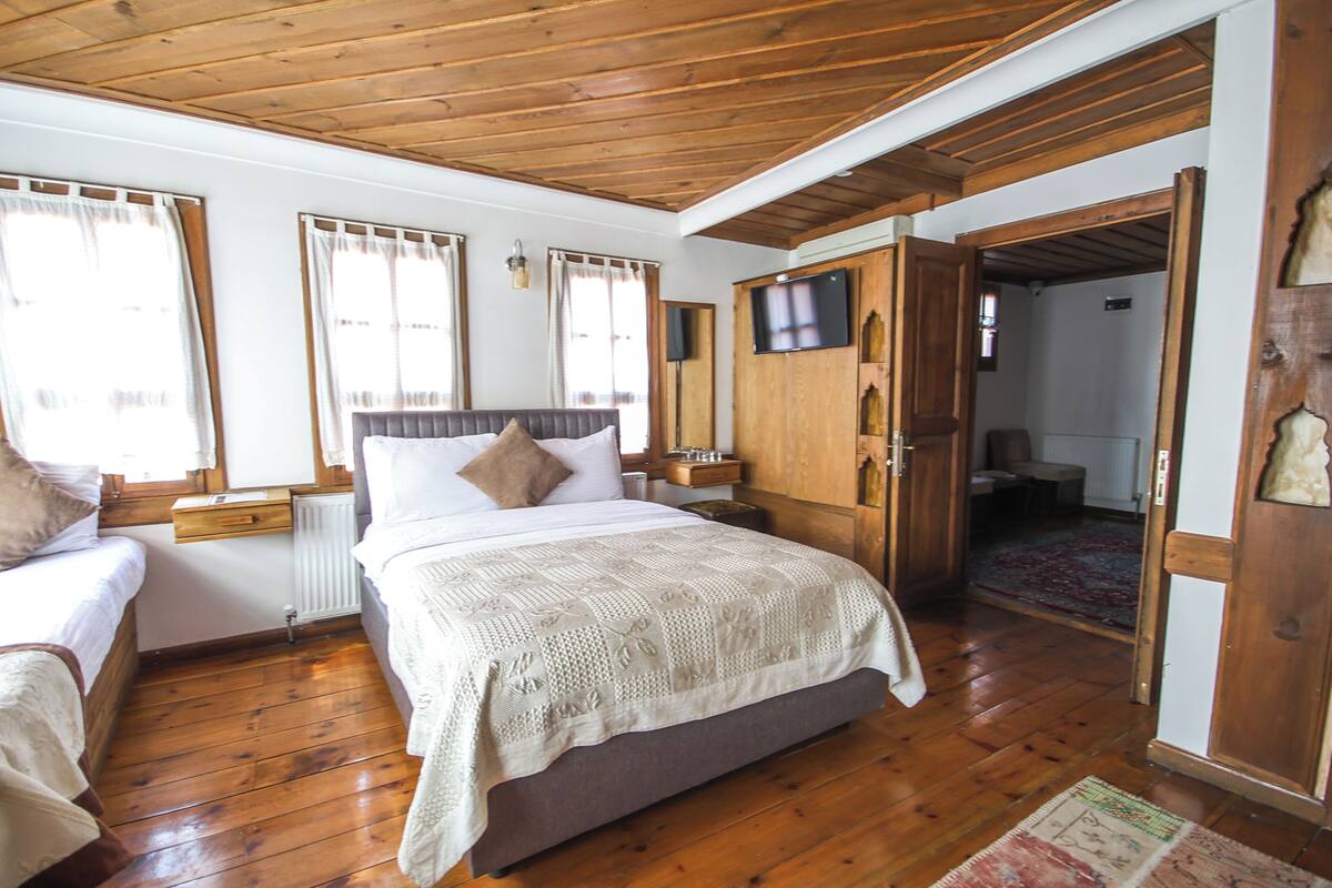 Une pièce avec un plafond en bois, un lit recouvert d’une courtepointe blanche, une armoire en bois et un téléviseur fixé au mur.