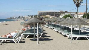 A beach with rows of sun loungers and thatched umbrellas, a hotel in the background, and a clear sky. - BALCON DEL MAR 2-3 A, APARTMENT ON THE BEACH FRONT (Mijas)