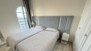 A double room with two beds, a nightstand, a lamp, a wardrobe, and a window with a view. - BALCON DEL MAR 2-3 A, APARTMENT ON THE BEACH FRONT (Mijas)