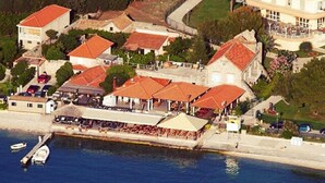 An aerial view of a coastal town with buildings, a waterfront, and a dock with boats. - Apartments Lotea (Konavle)