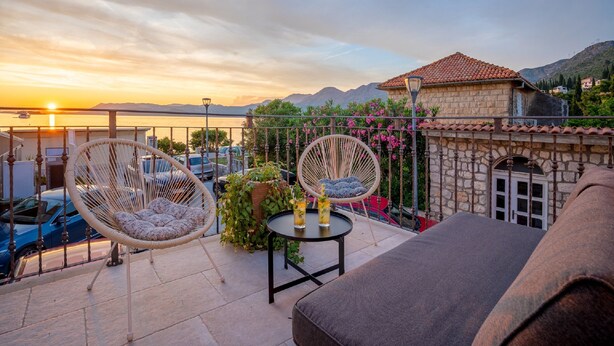 A terrace with wicker chairs, a table with drinks, and a view of the sunset over mountains. - Apartments Lotea (Konavle)