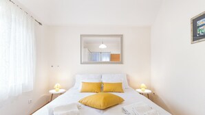 A neatly made bed with white and yellow bedding, two bedside lamps, and a mirror above the bed. - Apartments Lotea (Konavle)