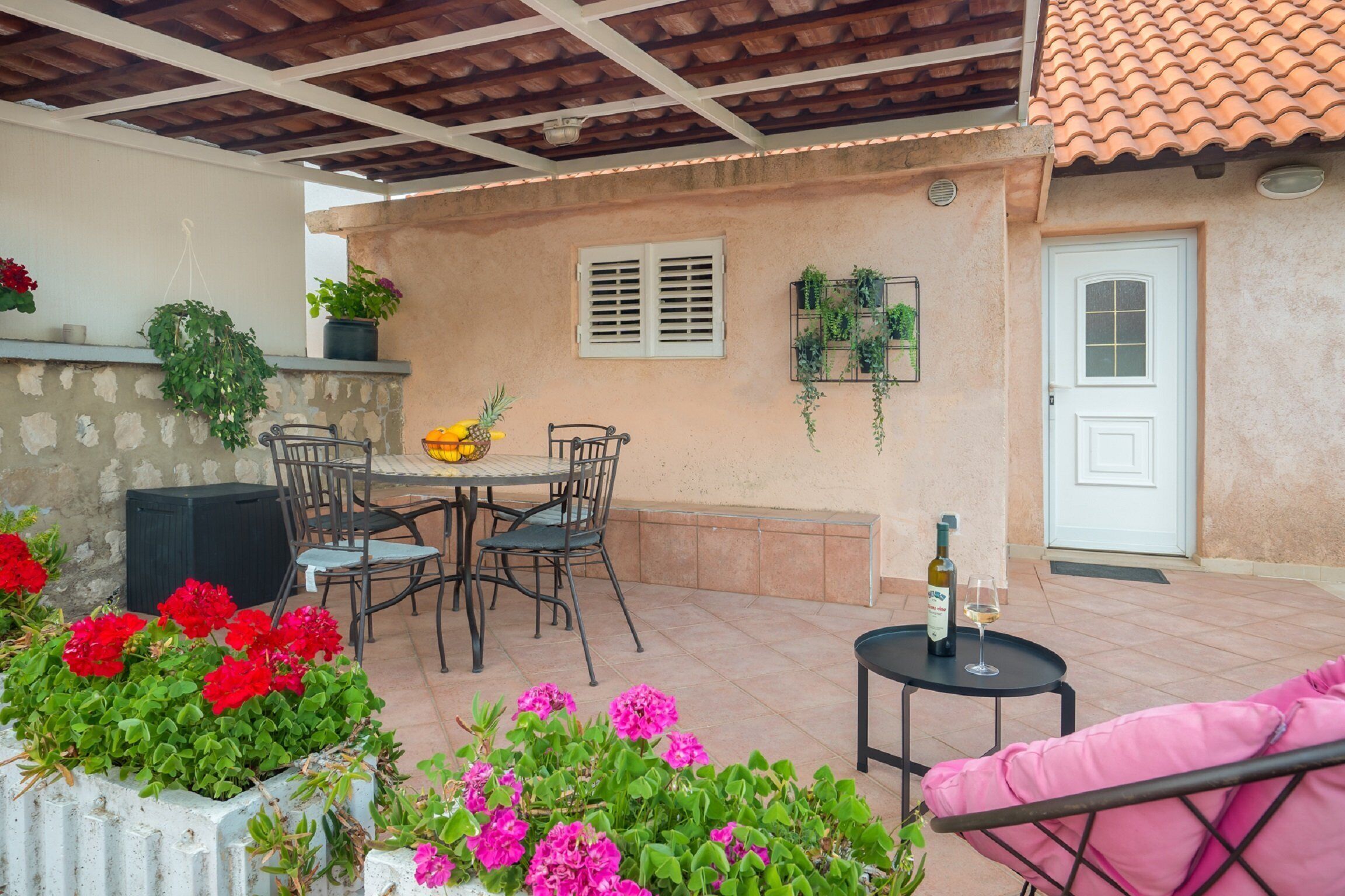 An outdoor patio area with a table and chairs, a small round table with a bottle and glass, and potted plants.