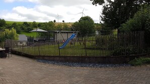 A paved patio area with a table and chairs, a covered seating area, and a fenced playground with slides. - Eifel Dream Landhaus (Plütscheid)
