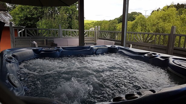 A hot tub with a wooden deck and a view of a lush green landscape. - Eifel Dream Landhaus (Plütscheid)