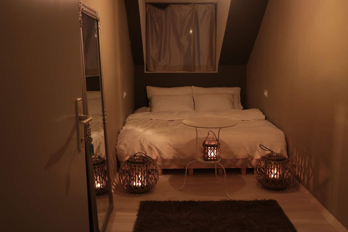 Ein Schlafzimmer mit einem Bett, Nachttischen, einem Spiegel und zwei beleuchteten Laternen.