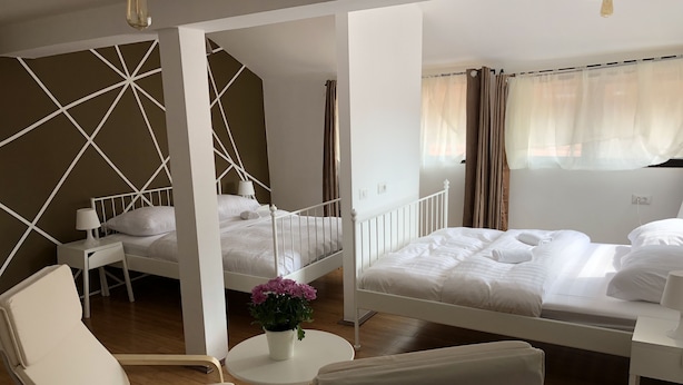 Ein Hotelzimmer mit zwei Betten, einem Sessel, einem kleinen Tisch mit Pflanze und einem Fenster mit Vorhängen.