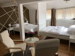 A hotel room with two beds, a chair, a small table with a plant, and a window with curtains. - Central Antique Apartments (Ljubljana)