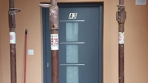Eine Tür mit dem Schild "A3", darüber eine Lüftung, ein roter Mop an der Wand angelehnt und ein roter Eimer auf dem Boden.