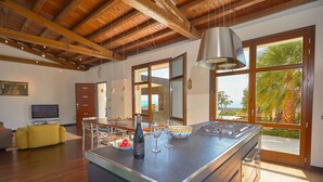 A modern kitchen with a large island, wooden ceiling beams, and a view of the outdoors.