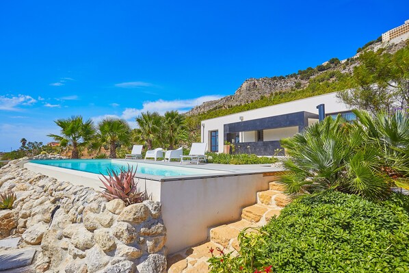 Et moderne hus med swimmingpool, omgivet af sten og planter.