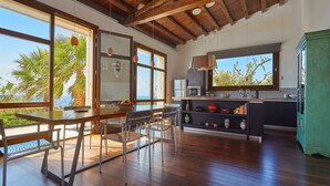 A spacious kitchen with wooden floors, large windows, and a view of palm trees.