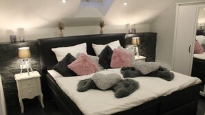 A modern bedroom with a black bed, white bedding, and decorative pillows. There is a small bedside table with a lamp, a wall-mounted shelf with decorative items, and a large mirror. - Eifel Dream Ardennenblick (Roth bei Prüm)
