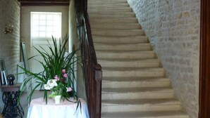A staircase with a stone wall on one side and a wooden railing. There is a table with a potted plant in the foreground. - Le Logis de Faugerit (Frontenay-Rohan-Rohan)