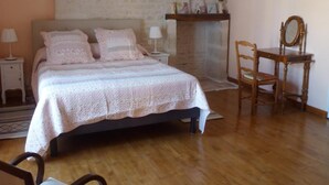 A bedroom with a bed, a chair, a nightstand, a lamp, and a fireplace. - Le Logis de Faugerit (Frontenay-Rohan-Rohan)