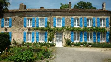 A two-story building with blue shutters, a gravel driveway, and a garden with various plants.
