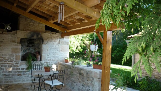 An outdoor patio with stone flooring, a stone fireplace, a wooden pergola, and potted plants. - Le Logis de Faugerit (Frontenay-Rohan-Rohan)