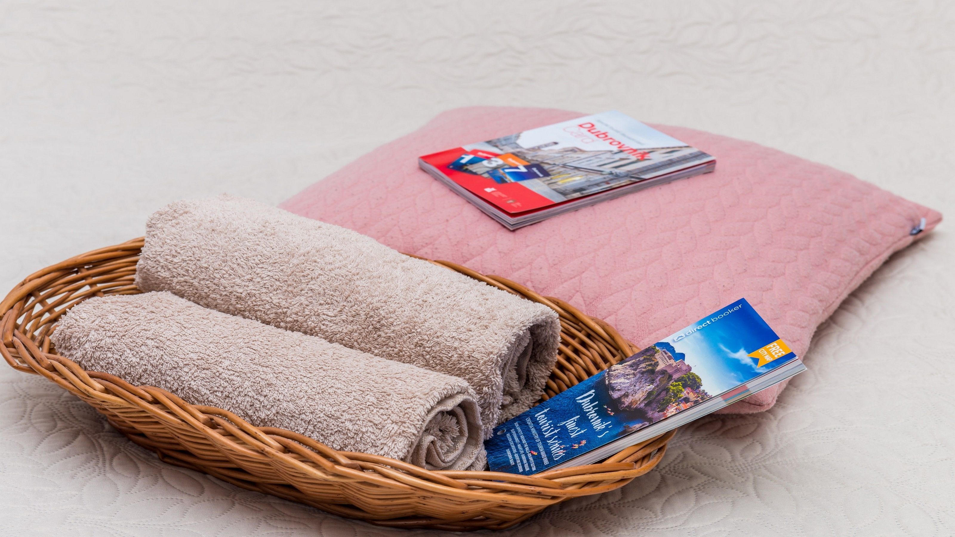 A wicker basket with rolled towels and a travel guidebook on a textured surface.