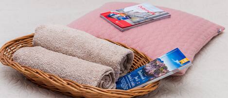 A wicker basket with rolled towels and a travel guidebook on a textured surface.