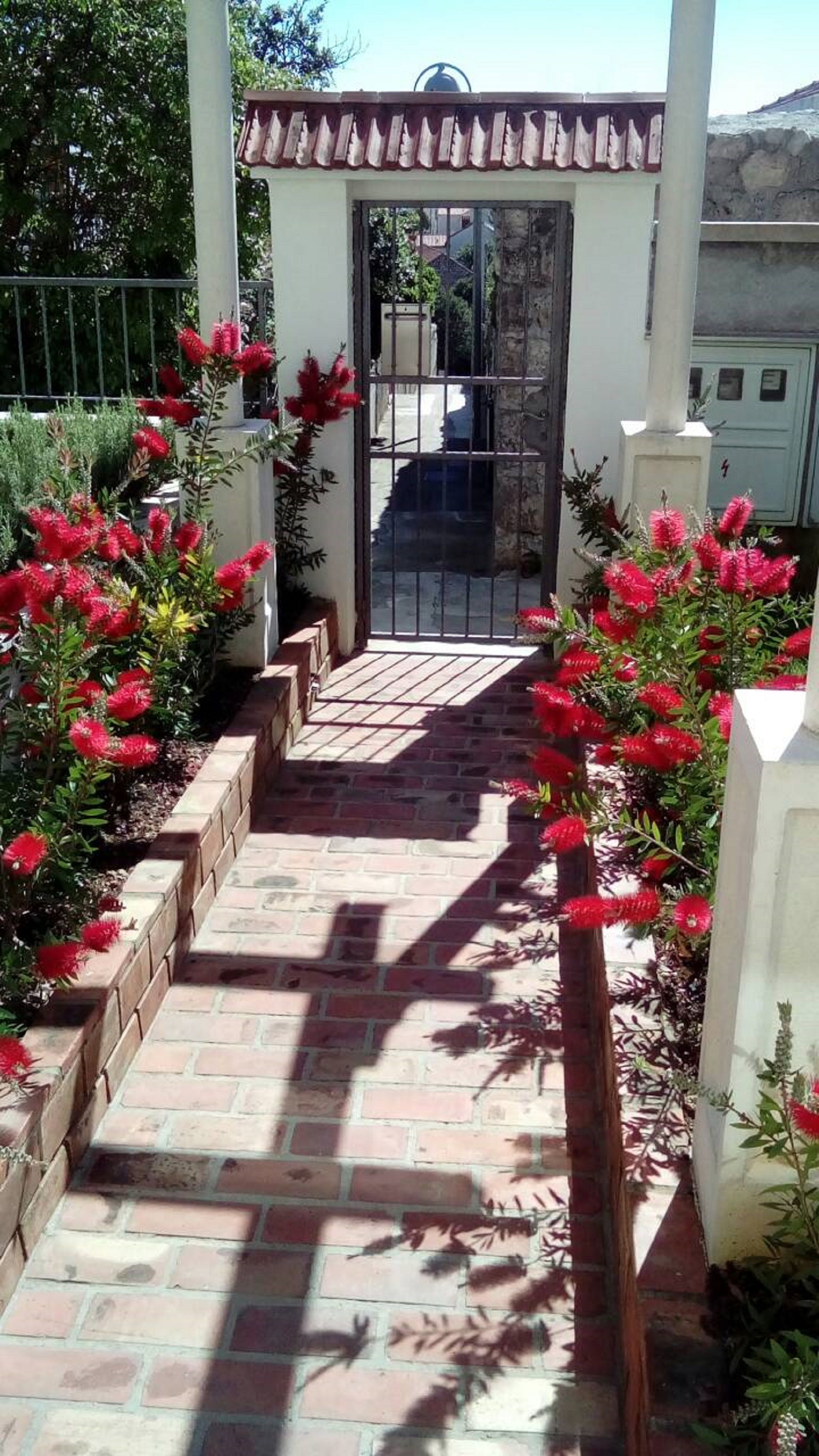 Un chemin pavé mène à une entrée fermée par un portail et surmontée d’un toit en tuiles.
