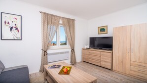 Quarto pequeno e bem iluminado, com janela, televisão de tela plana, armário de madeira e quadro na parede.