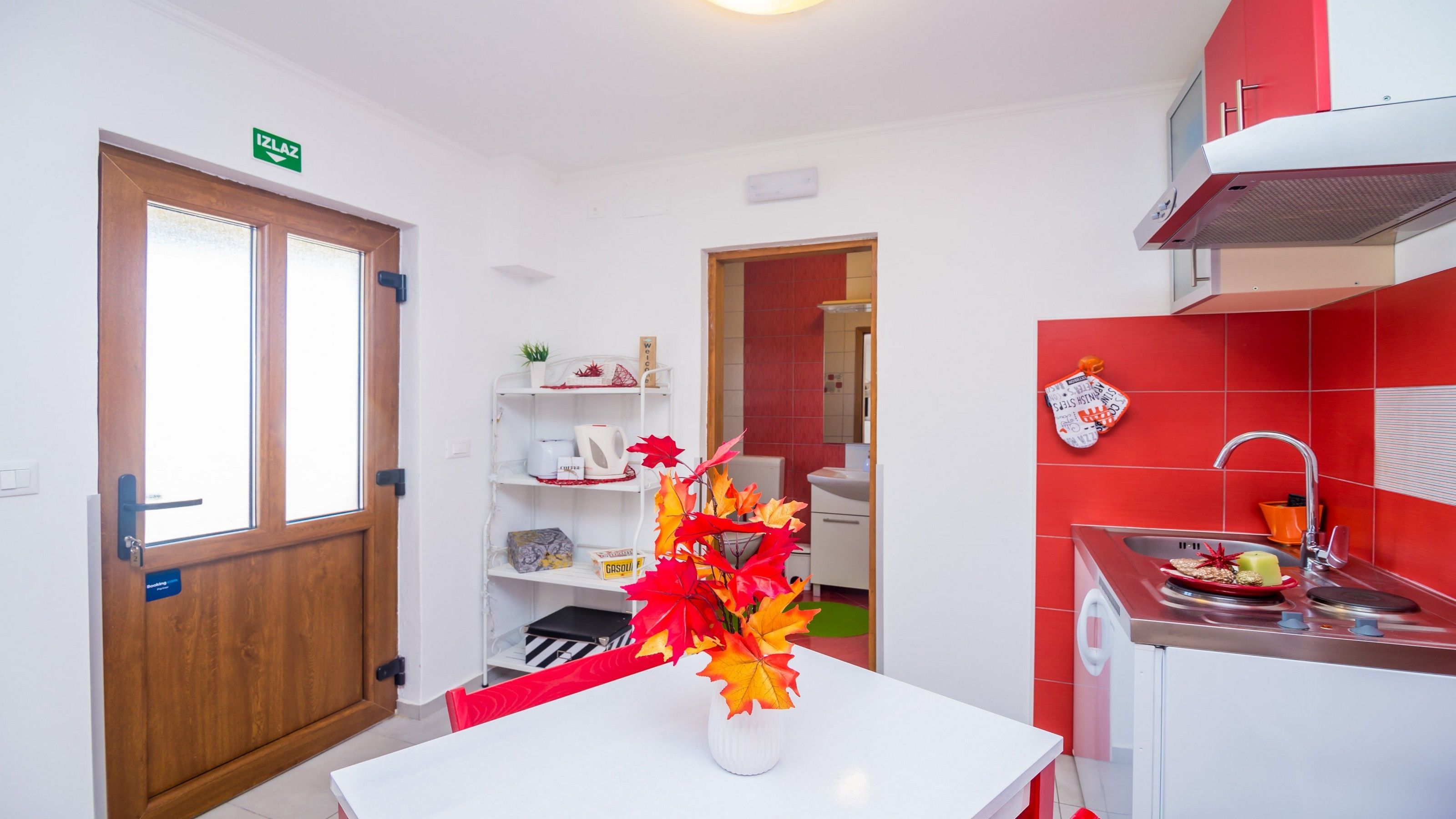 A modern kitchen with a red backsplash, white cabinets, and a white dining table with a vase of autumn leaves.