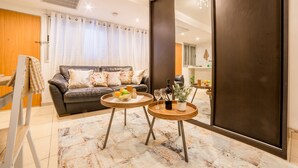 Una sala de estar moderna con un sofá de cuero, dos mesas redondas con bebidas y un espejo grande.