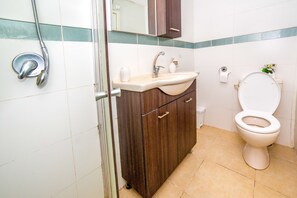 A bathroom with a shower, sink, cabinet, toilet, and a mirror.