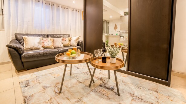 Una sala de estar moderna con un sofá de cuero, dos mesitas de madera, un tapete de mármol y un espejo grande.