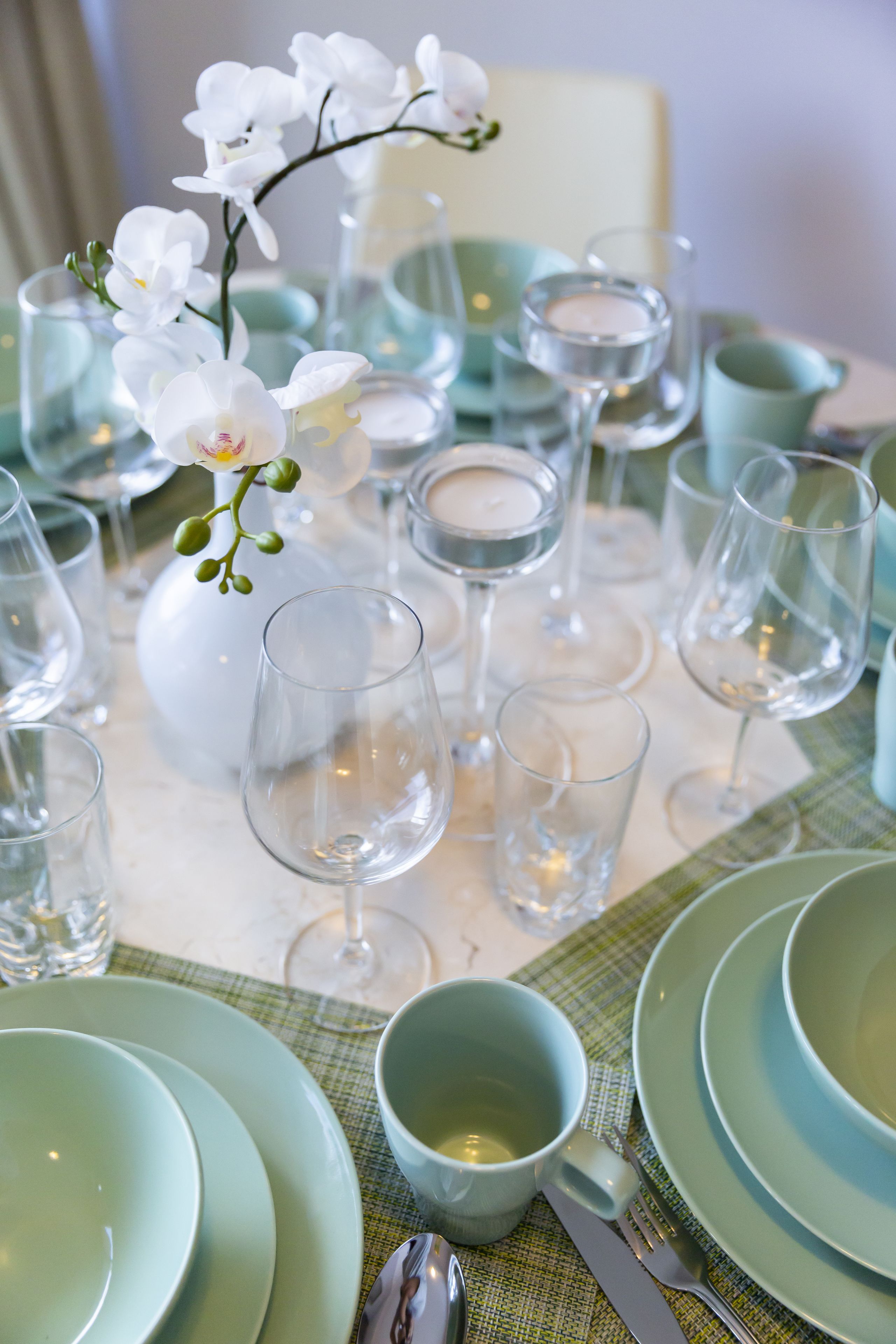 Une table dressée avec des assiettes vertes, des verres transparents et un vase blanc orné de fleurs.