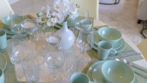 Un tavolo da pranzo apparecchiato con piatti, ciotole e bicchieri da vino, circondato da un divano bianco e un tavolino da caffè.