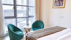 Una camera d'albergo con un'ampia finestra, due poltrone color petrolio, un tavolino rotondo e un letto con copriletto fantasia.