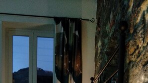 A bedroom with a bed, a nightstand, a lamp, and a window with curtains. - Arbanella (Vernazza)