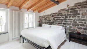 A bedroom with a stone wall, a wooden ceiling, and a bed with white bedding. - Arbanella (Vernazza)
