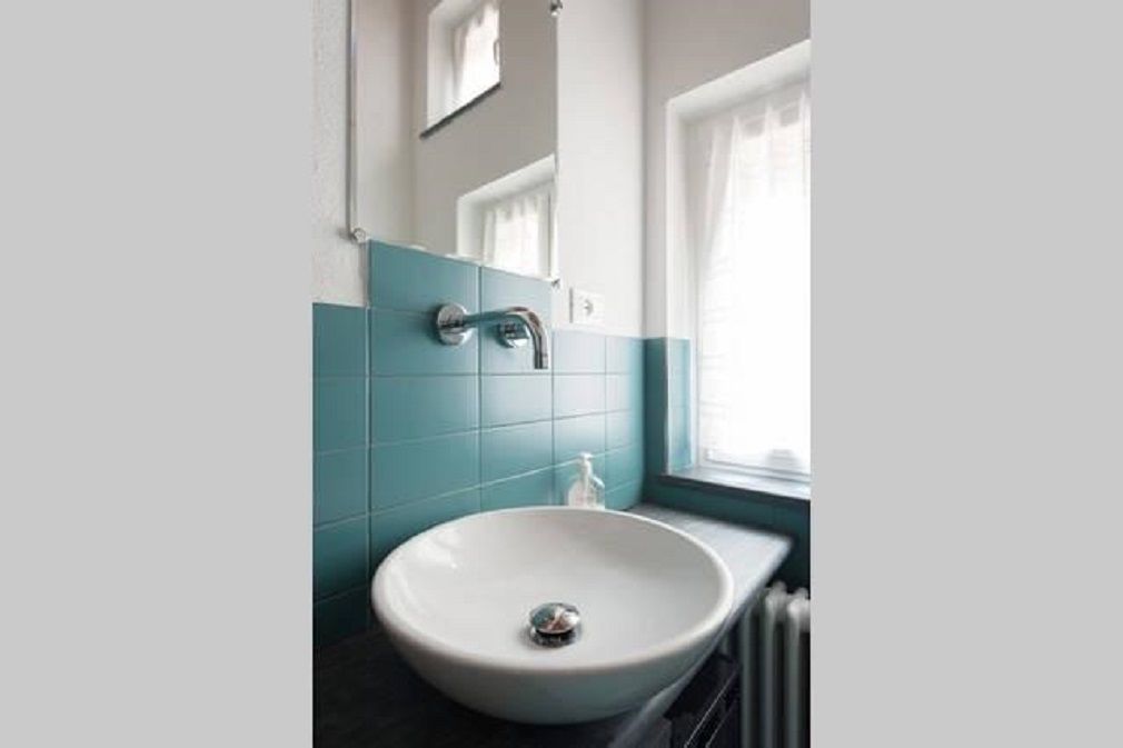 Un baño con un lavamanos blanco, azulejos verde mar, una ventana y un espejo.