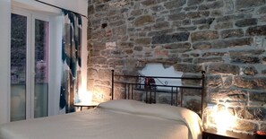 Ein Schlafzimmer mit Steinwand, einem Bett mit Metallkopfteil und einem Fenster mit Vorhängen.