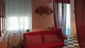 A cozy room with a red sofa, a small table, and a fan on the wall. - Onda su Onda (La Spezia)