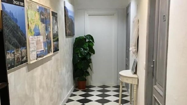 A hallway with a black and white checkered floor, a potted plant, a framed map on the wall, and a door on the right. - Onda su Onda (La Spezia)