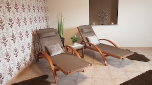 A room with two wooden lounge chairs with cushions, a small table with a potted plant, and a decorative tree on a shelf. - Eifel Dream Zingsheld (Fleringen)