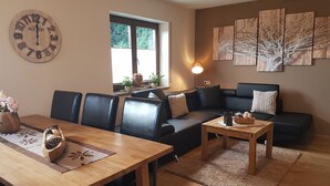 A living room with a wooden table, black leather sofa, and a wall clock. - Eifel Dream Zingsheld (Fleringen)