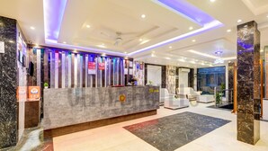 A modern hotel reception area with a marble reception desk, a seating area with white sofas, and a large TV screen. - Olivia Hotels @ Delhi Airport (New Delhi)