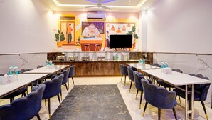 A conference room with a long table, chairs, a TV, and a kitchen area in the background. - Olivia Hotels @ Delhi Airport (New Delhi)