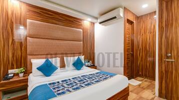 A bedroom with a large bed, wooden headboard, and a nightstand with a phone and a plant.